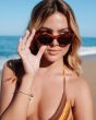 Mujer en la playa con gafas de sol I-SEA Carly Havana Tortoise Marrón levantando las gafas con una mano y mirando al horizonte.